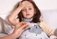 วิธีปกป้องลูกจากไข้หวัดใหญ่สายพันธุ์ใหม่ Subclade K Mother holding thermometer in hands, sick little girl lying in bed and keeping her palm on forehead, looks sad and upset, suffering from high temperature, needs treatment and examining by doctor.